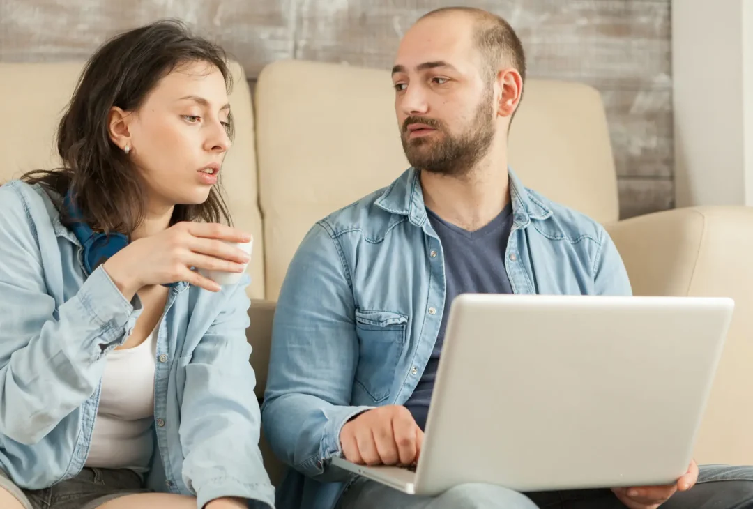 Couple relaxing in living room drinking coffee and browsing on internet.